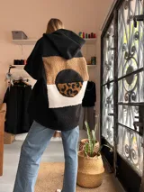 Campera tipo hoodie de textura tipo corderito en color negro, con diseño de collage en la espalda que combina parches en tonos marrón, blanco y estampado animal print de leopardo.