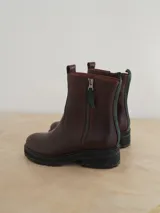 Botas de cuero color marrón chocolate con suela de goma tipo track en color negro. Presentan un diseño de caña media con cierre frontal metálico y costuras reforzadas.