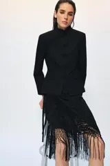 Falda corta de tiro medio, color negro, con diseño cruzado estilo pareo ajustable con lazada lateral. Cuenta con bordados tonales de motivos florales y bajo acabado con flecos largos.
