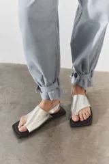 Sandalias de cuero plateado con diseño de dedo, base plana de color negro y tira trasera ajustable.