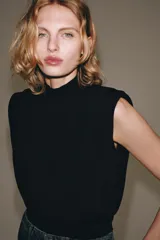 Top de punto negro sin mangas con cuello subido, hombreras y espalda descubierta.