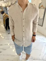 Camisa de lino a rayas beige y blancas, con cuello mao y cierre frontal de botones marrones, de manga larga.