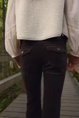 Pantalón acampanado de pana suave de algodón, color marrón oscuro. Presenta un corte ajustado de cintura a cadera y acampanado desde la rodilla al bajo. Es un modelo de tiro bajo con cierre y botón, con bolsillos abiertos delanteros y bolsillos traseros con solapa y botón.