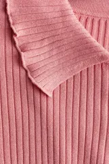 Buzo de punto acanalado color rosado, con cuello tipo polo, cierre frontal con botones nacarados, mangas largas y terminaciones con ribetes sobrehilados.