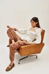 Camisa de algodón celeste con detalles de volados en los hombros y bordados en color negro en el pecho y las mangas. Presenta cierre frontal con botones y puños ajustados.