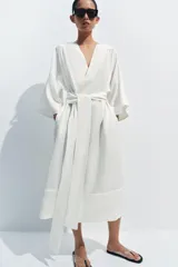 Vestido tipo túnica de corte evasé, color blanco, con escote en pico, mangas por debajo del codo y cinturón ajustable del mismo tejido.