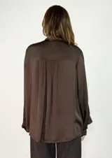 Camisa de satén color naranja óxido, con cuello mao y lazo para anudar. Presenta volados decorativos en el frente y en las mangas, las cuales son largas y terminan en puños abotonados.