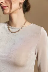 Top de manga larga con textura suave y leve brillo. Presenta una silueta al cuerpo, tajos laterales y terminaciones onduladas en el ruedo.