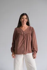 Blusa de color chocolate con cuello en V, cierre frontal con botones y mangas largas abullonadas. Presenta detalles de tablas en la parte superior y una costura horizontal con encaje decorativo en el pecho.