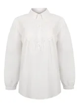 Blusa de algodón orgánico color blanco, con cuello camisero, cierre frontal parcial con botones y mangas largas. Presenta detalles de bordado inglés en el pecho y en los puños.