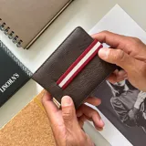 Billetera color beige de símil cuero lisa con galón elastizado marrón con línea blanca. Interior con doble repartición para billetes, visor y tarjeteros.