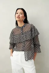 Camisa blanca de encaje bordado con diseño semitransparente, silueta fluida y mangas largas. Se destaca por los volados en el frente y hombros.