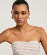 Top strapless color blanco roto con escote corazón y peplum fruncido en el bajo. El tejido presenta una textura acolchada o capitoneada.