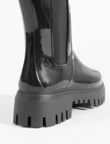 Botas de lluvia de caña media con acabado brillante, diseño tipo chelsea con paneles laterales elásticos en color negro y suela track dentada de plataforma.