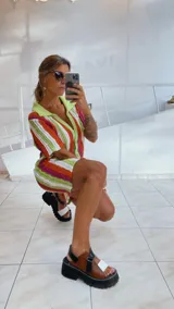 Vestido corto tejido calado a rayas horizontales en tonos naranja, amarillo y blanco, con cuello tipo polo y cierre frontal con botones.