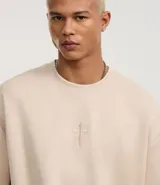 Remera oversized color beige confeccionada en gamuza sintética. Presenta cuello redondo, mangas cortas y bordado de cruz en el frente.