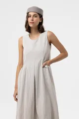 Vestido midi sin mangas de color beige, con silueta amplia y caída relajada, escote redondo y recortes frontales con volumen.