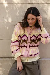 Saco tejido a mano con diseño jacquard geométrico en tonos rosa, amarillo y bordó. Presenta cuello a la base, cierre frontal con botones y silueta corta.