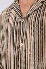 Camisa de manga corta con cuello solapa, corte holgado y cierre frontal de botones. Presenta un diseño de rayas verticales en tonos beige, negro y blanco.