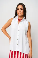 Camisa blanca sin mangas con cuello mao adornado con un delicado volado y cierre frontal con botones.