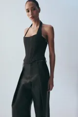 Top estilo corsé color beige, con escote recto, cuello halter y bajo asimétrico. Presenta costuras estructuradas frontales.