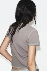 Camiseta de corte slim fit confeccionada en mezcla de algodón, con cuello redondo y manga corta. Presenta un detalle de texto bordado a contraste en la parte frontal.