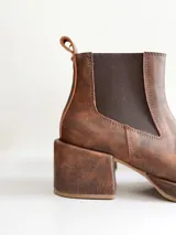 Bota tipo chelsea de cuero color chocolate con acabado texturizado, plataforma y taco cuadrado. Presenta paneles elásticos laterales en color negro.