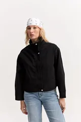 Campera de jean color negro, de calce amplio y largo a la cintura, con cuello alto y cierre frontal con broches a presión.