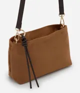 Bolso transversal Satinato de tamaño mediano, confeccionado en material sintético símil gamuza color marrón, con correa ajustable oscura, herrajes dorados y tiras decorativas colgantes con nudo.