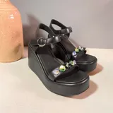Sandalias de plataforma negra con tacón de cuña, tira delantera decorada con piedras de colores y tira ajustable en el tobillo con hebilla metálica.