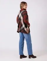 Polera estilo poncho de corte oversize, con cuello alto tejido y mangas largas con puños elásticos. Presenta un diseño de estampado a cuadros en tonos bordó, beige y negro.