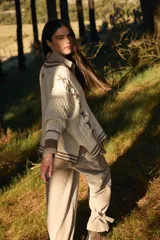 Sweater de punto estilo preppy en color crudo con detalles en marrón. Presenta cuello en V con ribete a rayas, tejido con textura de ochos y cordones laterales decorativos. Posee puños y ruedo acanalados con diseño a rayas.