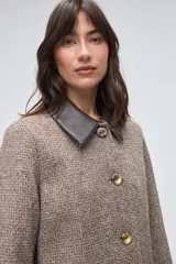 Tapado largo de lana fina con diseño de espiga en tonos beige. Presenta cuello camisero y solapas de bolsillos en cuero color suela, con cierre frontal de botones a tono.