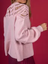 Sweater de punto color rosa con diseño de calados geométricos en la parte superior del pecho y hombros. Presenta cuello redondo, mangas largas con puños acanalados y un corte holgado.