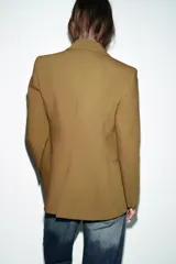 Blazer entallada de cuello solapa y manga larga con hombreras. Presenta bolsillos delanteros de vivo y cierre frontal con un botón metálico decorativo.
