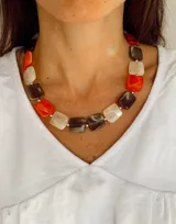 Collar de diseño geométrico compuesto por piezas rectangulares de resina en tonos naranja, marrón y crema, unidas por pequeñas cuentas metálicas plateadas.