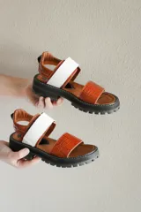 Sandalias de cuero color marrón con textura de cocodrilo, suela track color negro, tira ancha blanca y ajuste con hebilla.