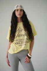 Remera amarilla de algodón con estampado frontal que incluye la frase 'Rio de Janeiro, a captivate journey, Copacabana, Icha Clothing since 2019'.