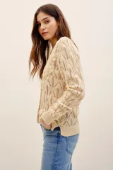 Cardigan de punto color beige con escote en V, cierre frontal con botones y detalles de flores bordadas en relieve a lo largo de la abertura. Cuenta con mangas largas y terminaciones en rib.