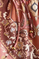 Blusa de viscosa con estampado paisley en tonos rojizos, cuello redondo con escote en V y tiras finas con cuentas decorativas. Cuenta con mangas globo largas terminadas en elástico fino y detalle de peplum acampanado en el ruedo.