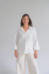 Camisa blanca de corte holgado con cuello clásico, cierre frontal de botones y mangas tres cuartos con sutil detalle bordado en los puños.
