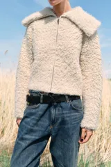Chaqueta de punto bouclé color crudo, con cuello de solapa grande, manga larga y cierre frontal con cremallera.