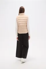 Chaleco acolchado negro, sin mangas, con cuello alto y cierre frontal con cremallera dorada. Presenta cordones ajustables a la altura de la cintura.