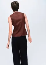 Chaleco de mezcla de lana color marrón oscuro, sin mangas, con cuello redondo, cierre frontal con botones y dos bolsillos de ribete delanteros. Presenta una abertura en el bajo frontal.