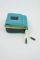 Billetera plegable color naranja con cierre de velcro y detalle de cordón marrón en el lateral. Presenta un parche negro con texto en relieve en la solapa frontal.