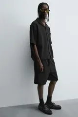 Bermuda de corte relajado color marrón con finas rayas verticales negras. Presenta cintura elástica ajustable con cordón y bolsillos laterales y trasero.