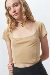 Top color beige de escote cuadrado y manga corta, con costuras verticales tipo corsé y leve brillo en la tela.