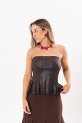 Top strapless de color marrón oscuro, confeccionado en tela engomada, con recortes verticales y falda plisada evasé en la parte inferior.