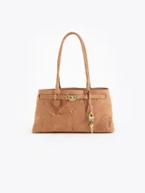 Cartera tipo tote de cuero vacuno marrón, con textura suave y silueta estructurada. Cuenta con asas largas para el hombro, detalle de tira frontal con hebilla metálica dorada y un candado con llave colgante como adorno.