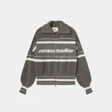 Campera de tejido de punto grueso, color verde militar, con cierre frontal y cuello tipo polo. Presenta franjas horizontales blancas y el logo "emestudios" en el pecho. Tiene un calce oversize y mangas abullonadas con puños y ruedo acanalados.